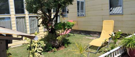 A residential backyard with a tree, a yellow chair, and a white fence.