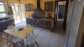 A compact kitchen with a dining area, a built-in oven, and a large refrigerator. - Maison aux Portes du Sud Sauvage – Family Home with Pool & Hot Tub (Saint Joseph)