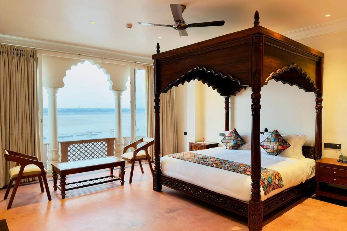 A four-poster bed with a view of the sea, a desk with a chair, and a nightstand with a lamp.