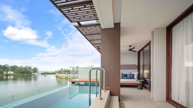 Ett modernt hotellrum med en glasbeklädd balkong med utsikt över en swimmingpool och en flod.
