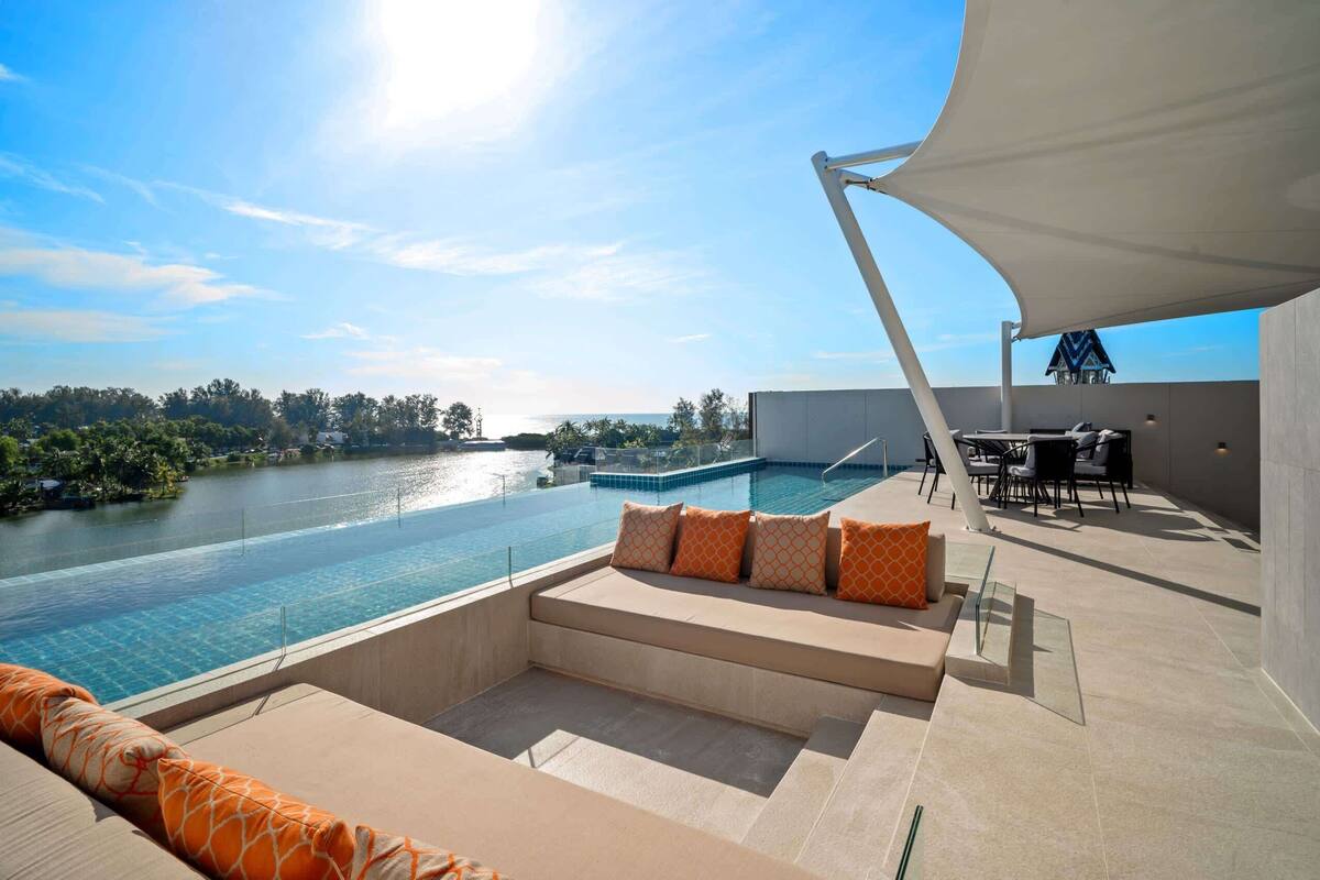 A rooftop pool area with a view of a river, outdoor seating, and a dining area.