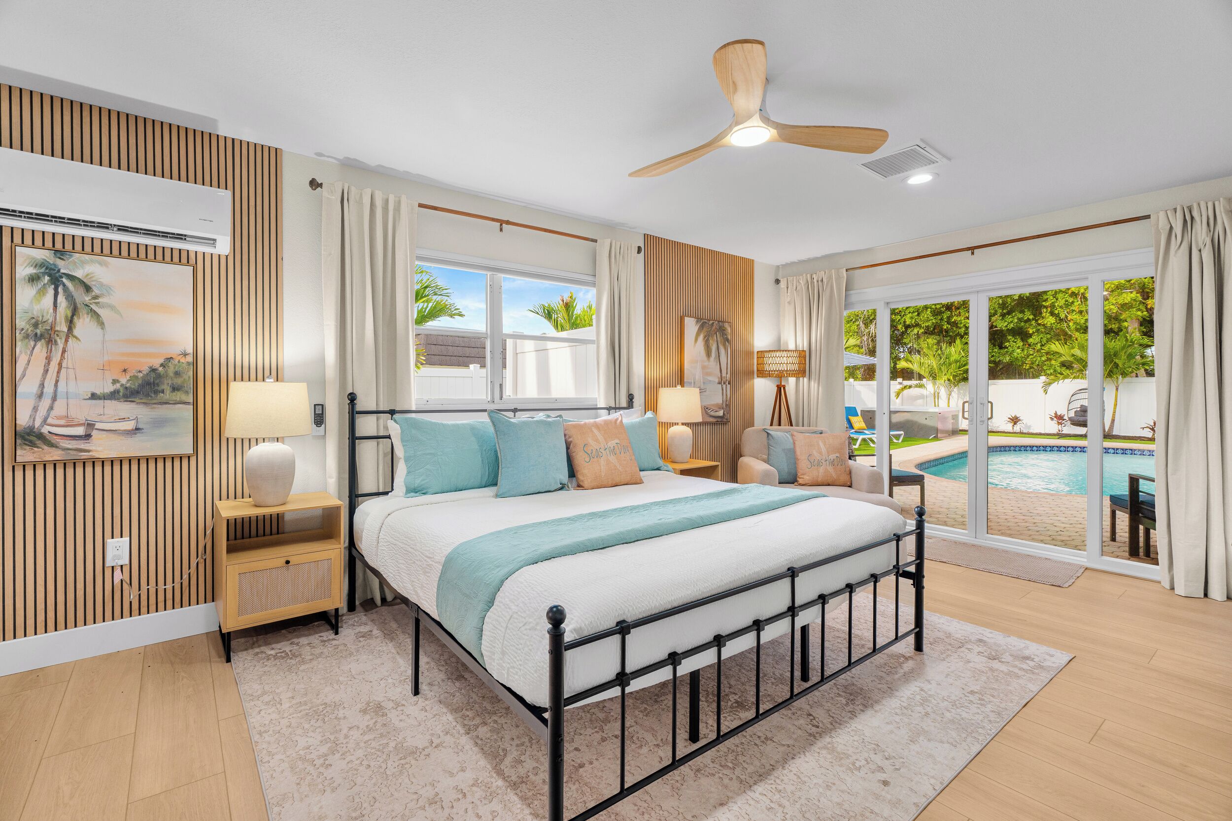 A bedroom with a bed, bedside tables, a ceiling fan, and a view of an outdoor pool area.