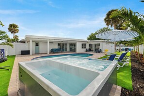 Ein Swimmingpool mit Whirlpool, Liegestühlen und Palmen.