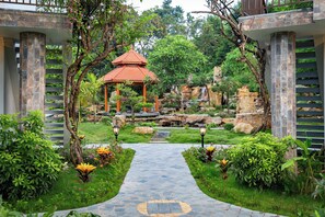 A garden pathway leading to a gazebo, surrounded by lush greenery and stone structures.
