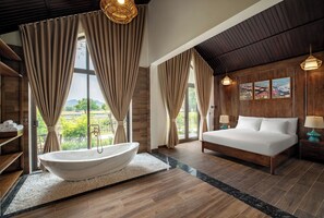A spacious bedroom with a large bed, a bathtub, and a view of greenery.