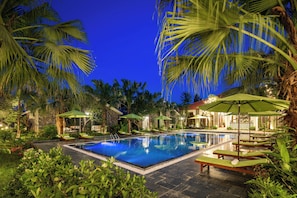 A swimming pool with lounge chairs and umbrellas, surrounded by palm trees and greenery.