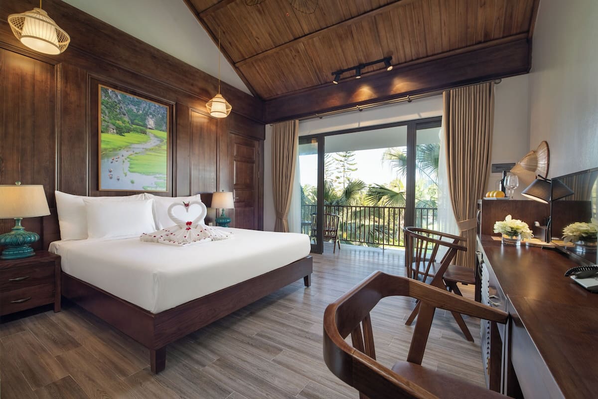 Une chambre d’hôtel avec un grand lit, un bureau, une chaise, un balcon avec vue et un tableau au mur.