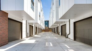 Pitkä käytävä, jossa on useita ovia, vasemmalla tiiliseinä ja yläpuolella kirkas taivas.