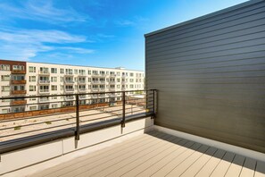 Ein Balkon mit Metallgeländer, Blick auf ein mehrgeschossiges Gebäude und einen klaren Himmel.
