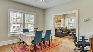 Un coin repas avec une table, des chaises et un tapis rouge. On aperçoit un canapé et un bureau au fond.