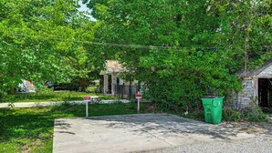 A concrete driveway leading to a building with a stone facade, surrounded by lush greenery and a green trash bin. - Charlotte Duplex Close to Uptown and Sports (Charlotte)