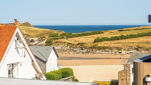 A coastal view with a beach, grassy hills, and a white building with a red roof. - Seascape (Newquay)