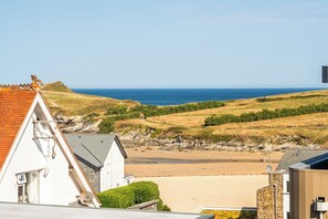 Blick auf die Küste mit Strand, grünen Hügeln und einem weißen Gebäude mit rotem Dach.