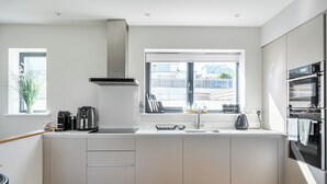 A modern kitchen with a window, built-in oven, and a coffee machine. - Seascape (Newquay)
