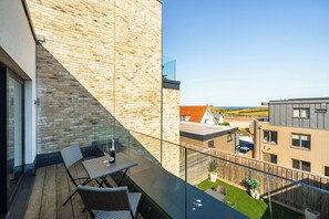 Ein Balkon mit Meerblick, einer Holzterrasse und einem Glasgeländer.