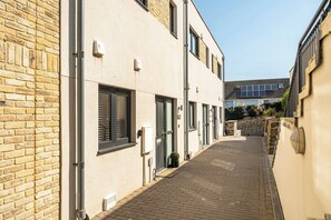 A narrow alleyway with a brick pathway, a building with a brick facade, and a modern building with solar panels in the background. - Seascape (Newquay)