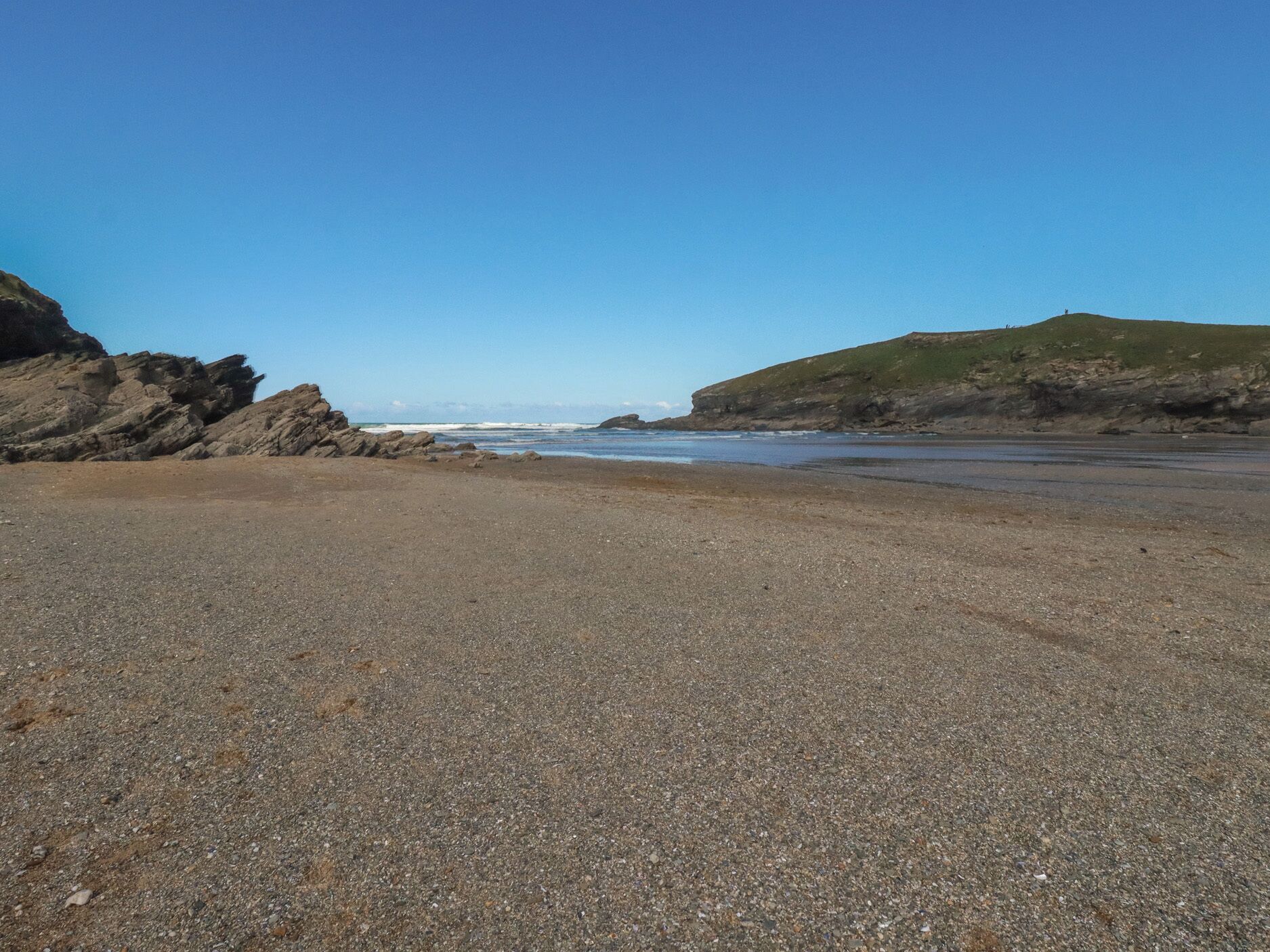 A pebbly beach with rocky cliffs and a clear sky.