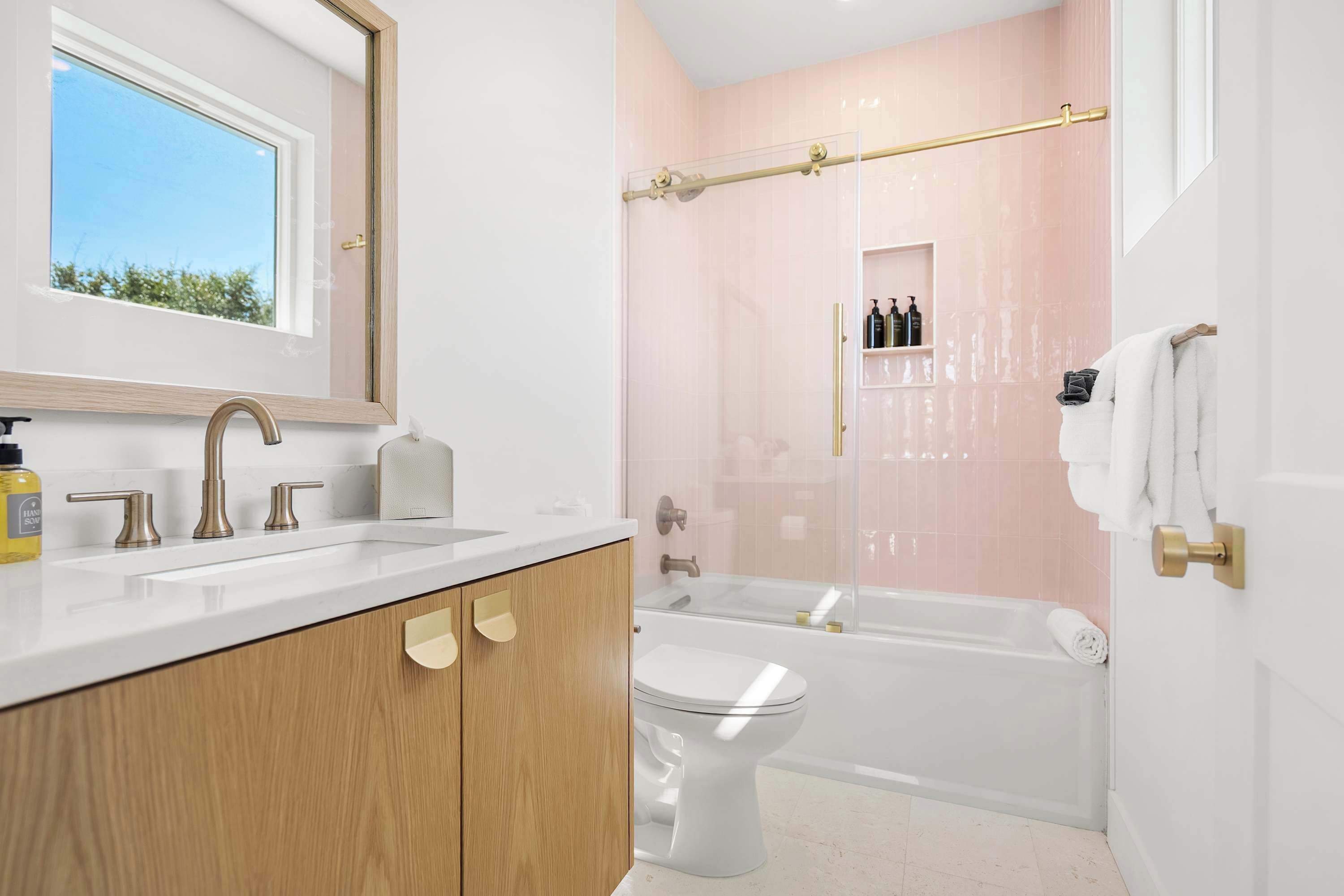 A modern bathroom with a large window, a bathtub, a toilet, and a vanity with a mirror.