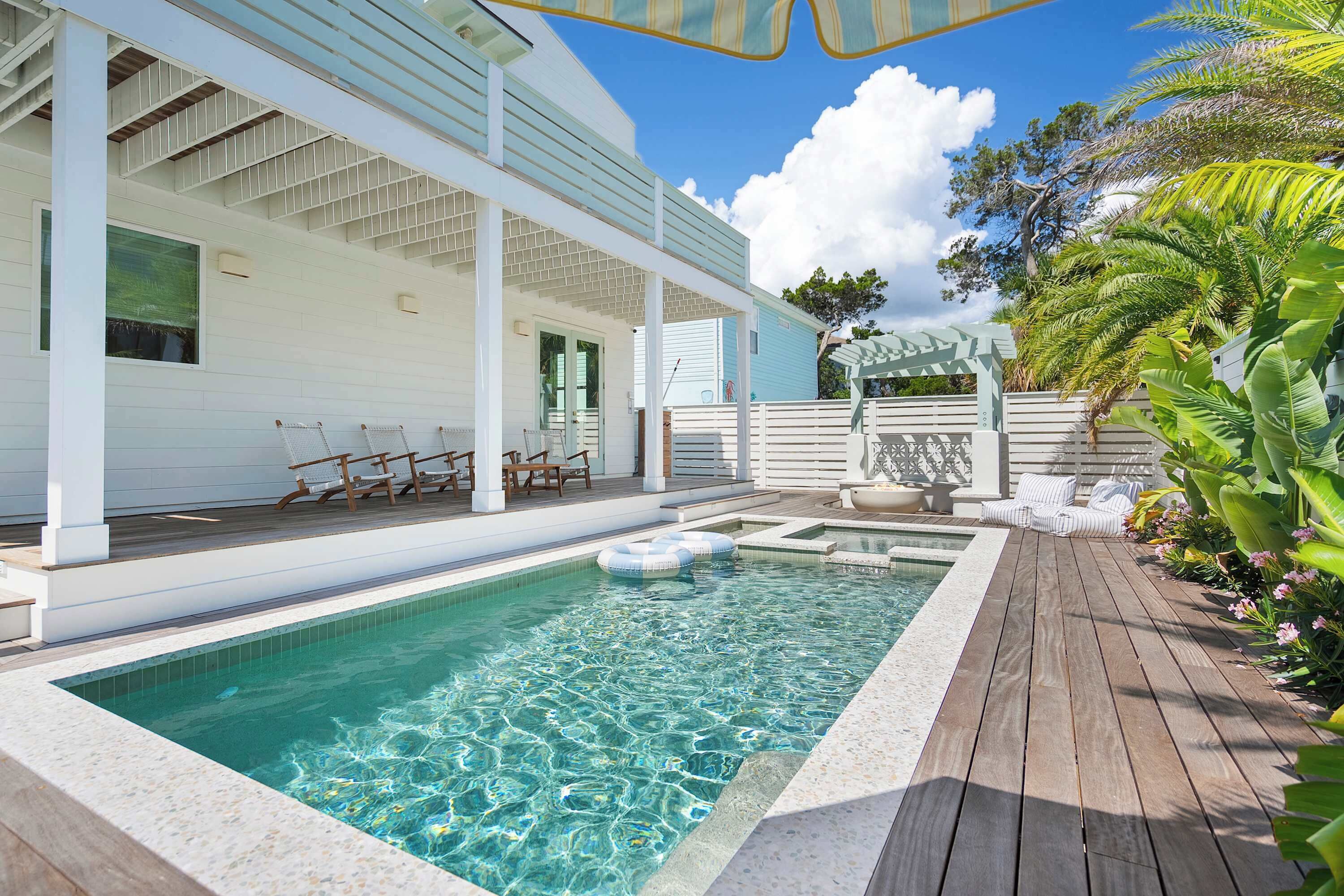 Una piscina con bordo in legno, poltrone da relax e un'area patio coperta.