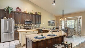 A kitchen with a central island, bar stools, a refrigerator, and a dining area with a view. - Hot Tub, Game Room! Ozarks Family Retreat By Lake (Eldon)
