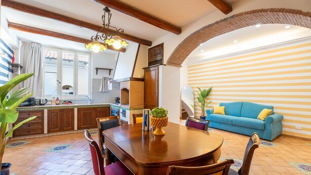 Ein Essbereich mit Holztisch und Stühlen, einem blauen Sofa und einer Küche im Hintergrund.