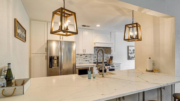 A kitchen with a marble countertop, stainless steel appliances, and hanging pendant lights. - Lake Conroe Waterfront in Walden! Lovely 4 Bdrm! (Montgomery)