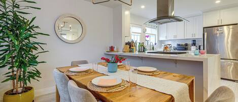 A modern kitchen with stainless steel appliances, a dining area with a wooden table and chairs, and a potted plant.