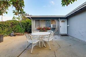 Eine Terrasse mit rundem Tisch und Stühlen, eine weiße Tür und ein kleiner Garten mit einer Statue und Topfpflanzen.