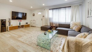 Un salon comprenant un canapé, une table basse en verre, un téléviseur à écran plat et un meuble en bois.