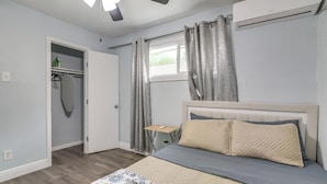 Ein Schlafzimmer mit Bett, Deckenventilator, Klimaanlage, Fenster mit Vorhängen, Nachttisch und Kleiderschrank.