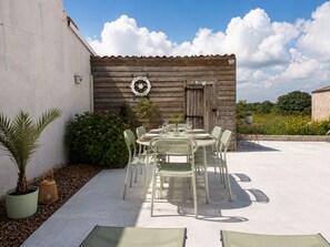 Eine Terrasse im Freien mit einem Tisch für vier Personen, umgeben von Stühlen, vor einer rustikalen Holzwand mit einem Schild darüber.