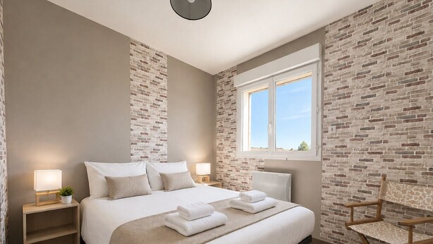 Quarto com uma cama grande, duas mesas de cabeceira, uma cadeira, uma janela e paredes com padrão de tijolos.