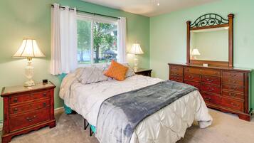 Une chambre à coucher comprenant un lit, deux tables de chevet, une commode, un miroir et une fenêtre avec des rideaux.