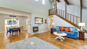 Ein geräumiges Wohnzimmer mit einer Holztreppe, einem Essbereich mit Tisch und Stühlen sowie einem blauen Sofa mit orangefarbenen Kissen.