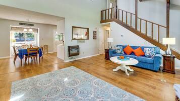 Un vaste salon agrémenté d’un escalier en bois, un coin repas avec une table et des chaises, et un canapé bleu avec des coussins orange.