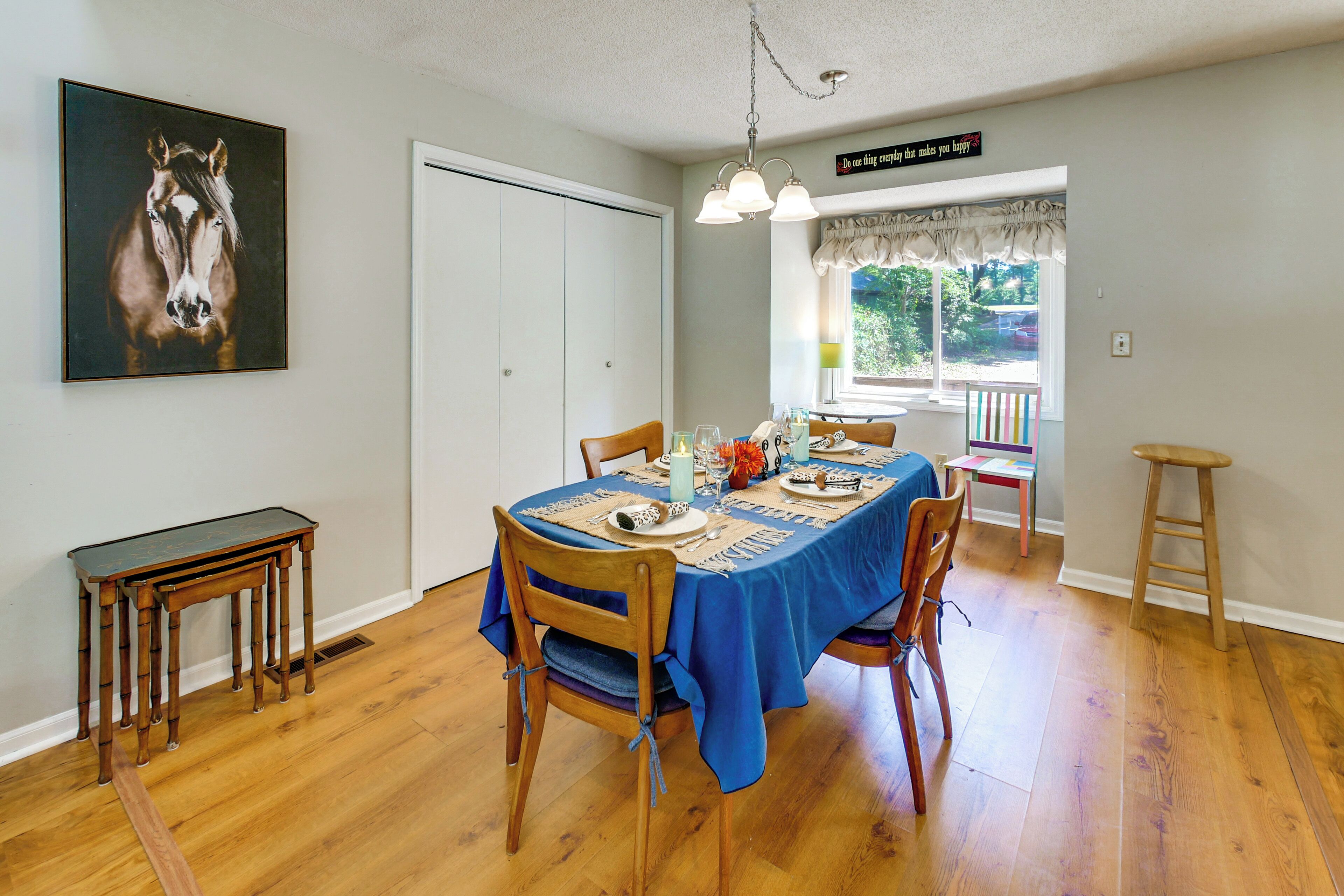 Un coin repas avec une table dressée pour quatre personnes, une chaise en bois, une petite table et un tableau accroché au mur.