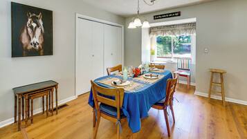 Un coin repas avec une table dressée pour quatre personnes, une chaise en bois, une petite table et un tableau accroché au mur.