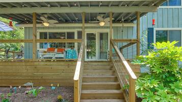 Une terrasse en bois avec un escalier menant à un espace abrité, doté d’un ventilateur de plafond et d’éclairages.