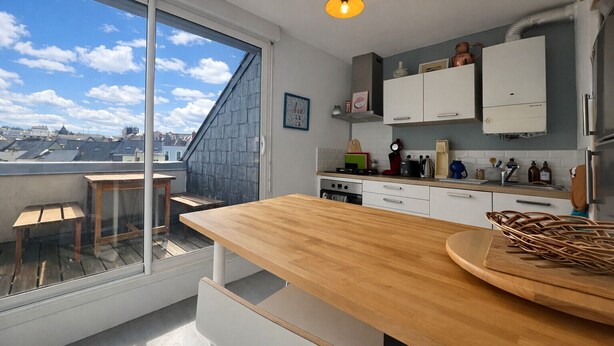 Une cuisine moderne dotée d’une grande fenêtre, d’un comptoir en bois et offrant une vue sur le paysage urbain.