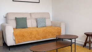 Un salon avec un canapé, deux tables d’appoint, un tapis jaune et une carte encadrée accrochée au mur.