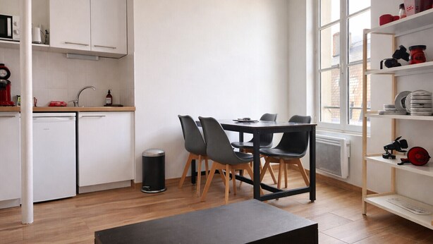 A modern kitchen with white cabinets, a dining table with chairs, a black trash bin, and a window with a view of the outside. - Comfortable apartment for 2 guests in the historic district - Cinema getaway (Angers)