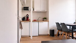 A compact kitchen with a microwave, coffee maker, and sink, a dining area with chairs, and a trash can. - Comfortable apartment for 2 guests in the historic district - Cinema getaway (Angers)