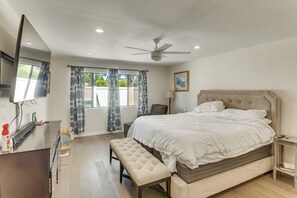 Ein Schlafzimmer mit einem Bett, einer Bank, einem Fernseher, einem Deckenventilator und einem Fenster mit Vorhängen.