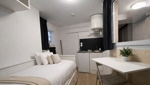 A compact room with a bed, a small kitchenette, a desk, and a potted plant. - Comfortable and cozy studio – 2 people – La Doutre district, Angers (Angers)