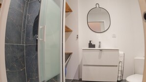 Moderni kylpyhuone, jossa on lasiseinällä varustettu suihku, valkoinen pesuallas ja wc.