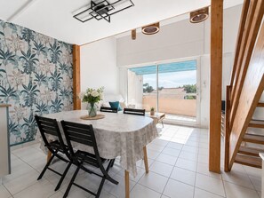 Ein Essbereich mit Tisch, Stühlen, einem Blumenstrauß und Blick durch eine Glastür auf einen Balkon.