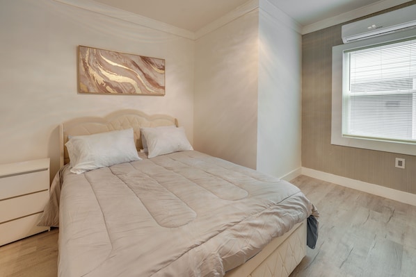A bedroom with a bed, a nightstand, a wall-mounted artwork, and a window with blinds.