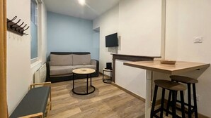 Un espacio habitable compacto con sofá, una pequeña mesa redonda, una barra y un televisor montado en la pared.