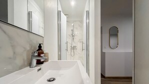 Un baño moderno con un lavamanos grande de color blanco, un cabezal de ducha de mano y una ducha con cerramiento de vidrio.