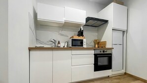 Una cocina compacta con armarios blancos, microondas, estufa y refrigerador.
